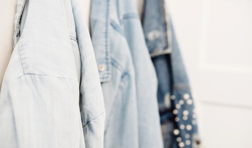 The image shows three light blue denim jackets hanging in a row on hooks. The denim jackets have a casual, worn-in look, with one featuring white polka dots. The photo highlights the texture and style of the denim fabric,