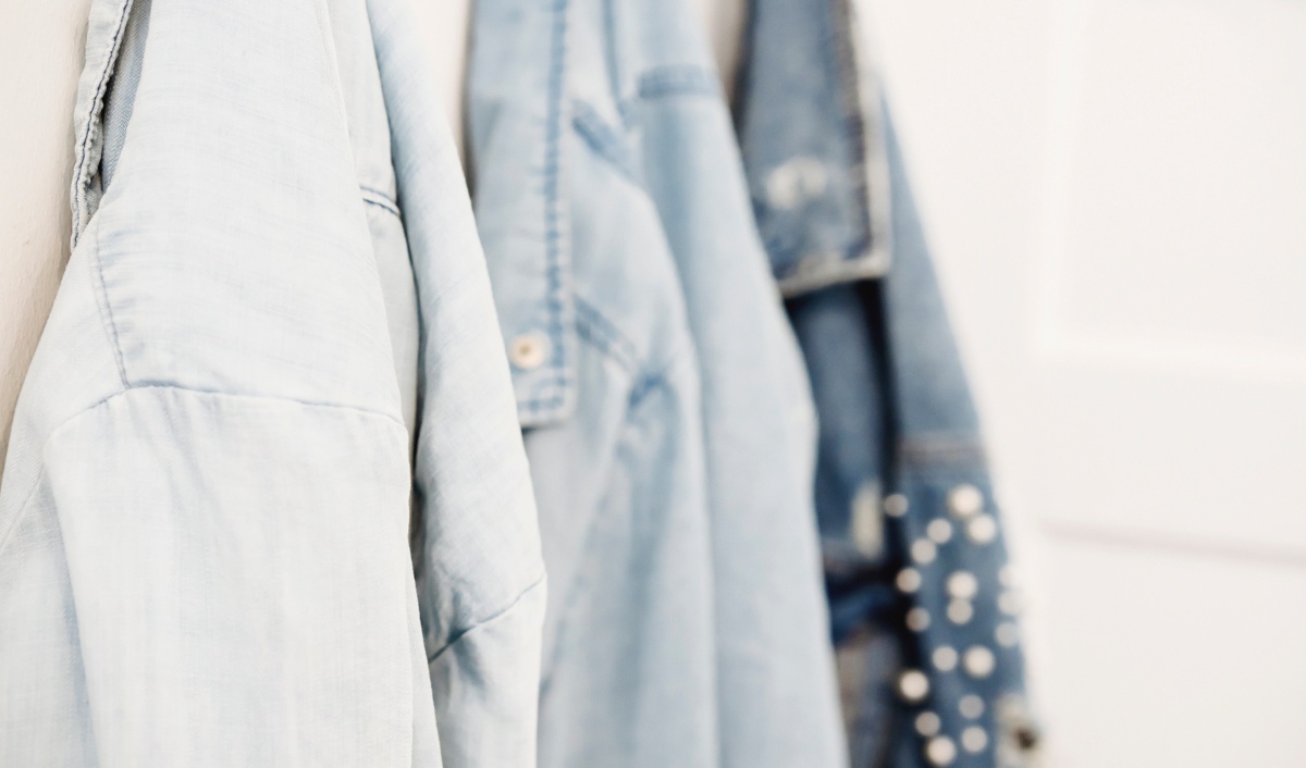 The image shows three light blue denim jackets hanging in a row on hooks. The denim jackets have a casual, worn-in look, with one featuring white polka dots. The photo highlights the texture and style of the denim fabric,