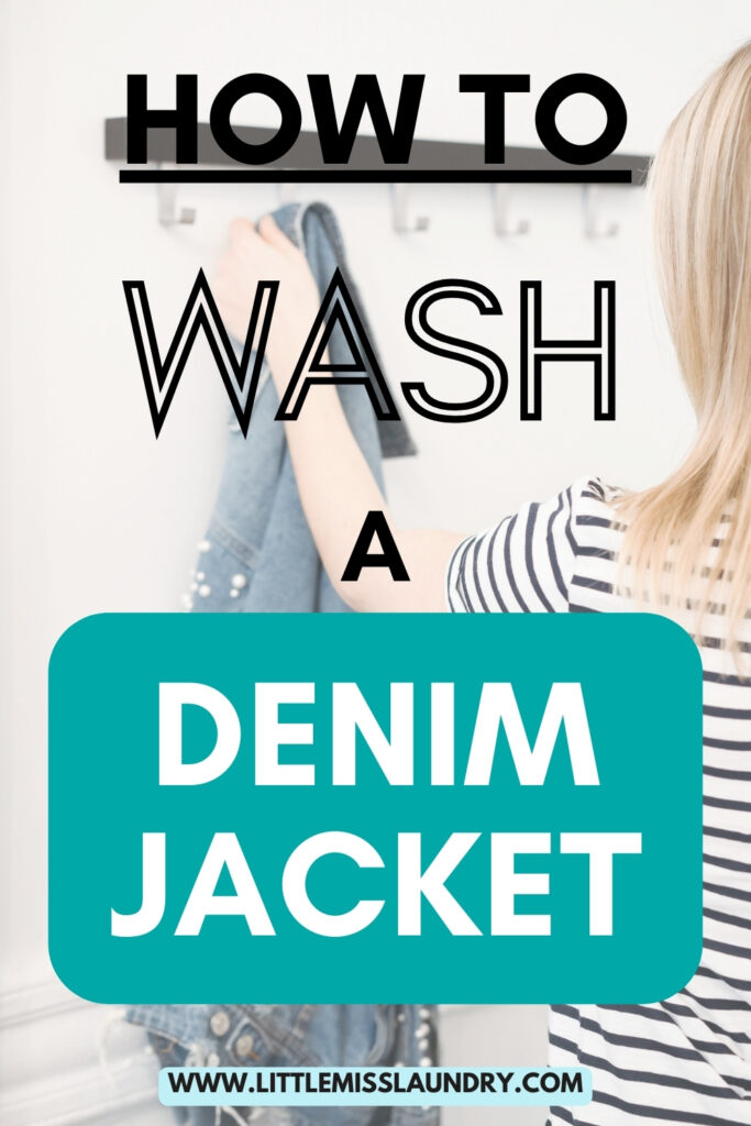 The image features the text "How to Wash a Denim Jacket" in bold, stylized fonts overlaid on a photo of a person hanging a denim jacket on a wall hook. The person is wearing a striped shirt and the bottom of the image includes a website URL, littlemisslaundry.com. 